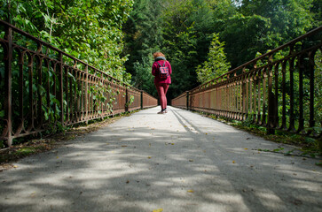 Femme rousse avec des vêtement rouge marchant sur un pont aux barrière rouillé dans la nature