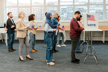 Group of multinational US citizens, voters standing in line to polling booth with American flag