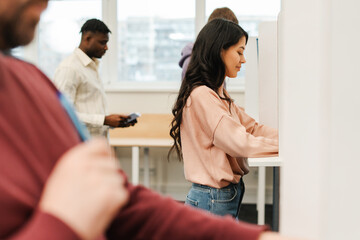 Obraz premium Smiling, beautiful, Asian young woman standing in voting booth with American flag, voting