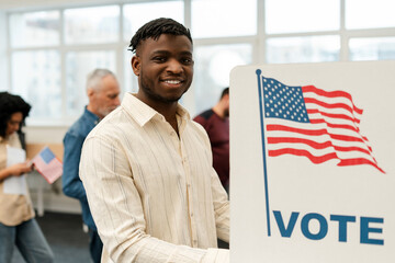 Handsome smiling African American man, voter standing in election booth voting, looking at camera