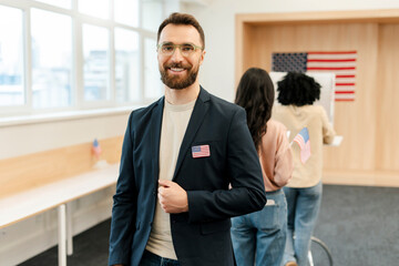 Smiling, bearded middle-aged man, voter wearing eyeglasses standing in line at polling station