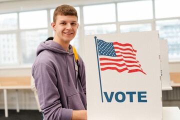 Attractive, young guy, American voter standing near a booth with an American flag looking at camera