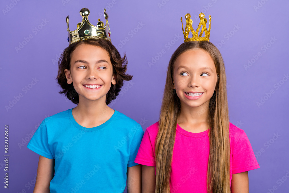 Poster Photo of cheerful tricky friends wear t-shirts golden crowns looking each other isolated violet color background