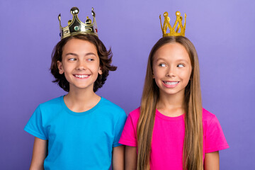 Photo of cheerful tricky friends wear t-shirts golden crowns looking each other isolated violet...