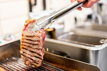 Hand grilling a juicy steak with tongs on a grill pan in a well-lit kitchen, with various kitchen...