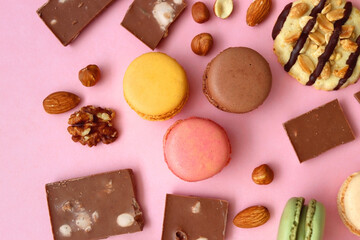 Pastel macarons, almond chocolate, peanut butter cookies and various nuts on bright pink background. Top view.