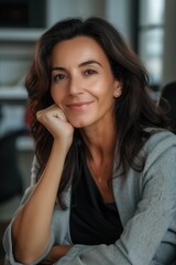 Portrait of a charming elegant mature middle-aged brunette stylish middle aged businesswoman sitting in light office touch her chin and smiling at camera, sitting wearing casual clothes