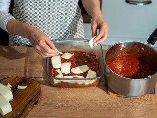 Arranging Italian mozzarella cheese in a glass dish, Italian dish lasagna, wooden base, female hands hold pieces of white mozzarella cheese