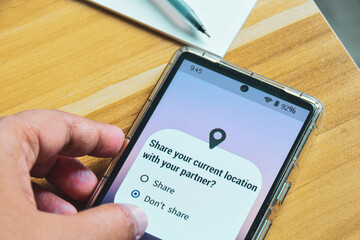 Mobile phone screen displaying the message Share your current location with your partner. Person decision not to allow it. Relationship trust issues concept.