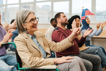 Smiling, senior, mature woman holding American flag, cheering for candidate, sitting in wheelchair