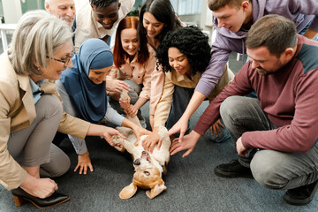 Group of smiling business people, multinational men and women petting dog while sitting on floor