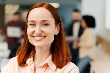 Portrait smiling, beautiful woman, ginger businesswoman looking at camera standing in modern office
