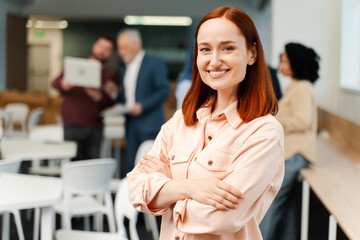 Cheerful, smiling woman with arms crossed looking at camera working in modern office, closeup