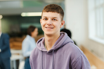 Young smiling man, IT specialist, student working in modern office, standing on university campus