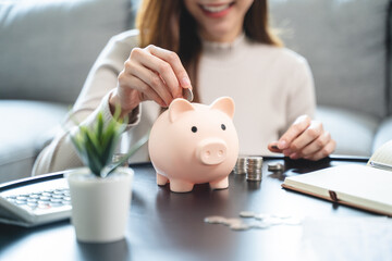 Young woman saving money monthly expenses putting coin in to piggy bank on the table.