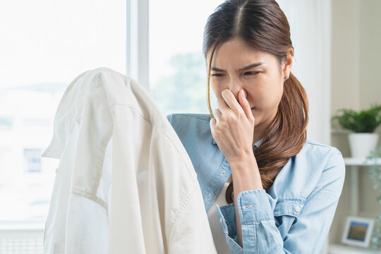 Smelly clothes laundry, housewife woman having bad smelling clothes on the hand holding breath nose with finger, sniff smelly dirty stinky musty and look disgusting.