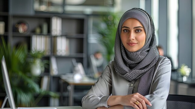 Professional Middle Eastern woman working in a modern office setting, seated at a desk with a backdrop of innovation and forward-thinking design.
