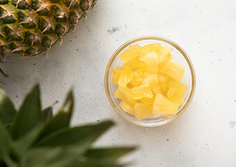 Dried soft sweet pineapple slices in glass bowl with raw pineapple on light table.Top view.