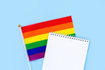 Blank mock up notebook on rainbow LGBTQ flag, blue background. June proud pride month parade, gay marriage, coming out day , human rights, tolerance concept. Flat lay, top view place for text or logo