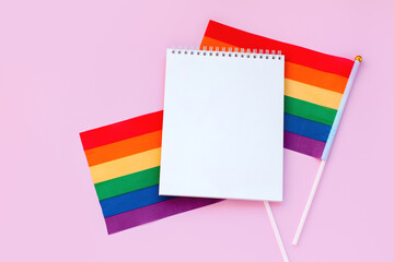 Blank mock up notebook on rainbow LGBTQ flag, pink background. June proud pride month parade, gay marriage, coming out day concept, human rights, tolerance. Flat lay, top view place for text or logo