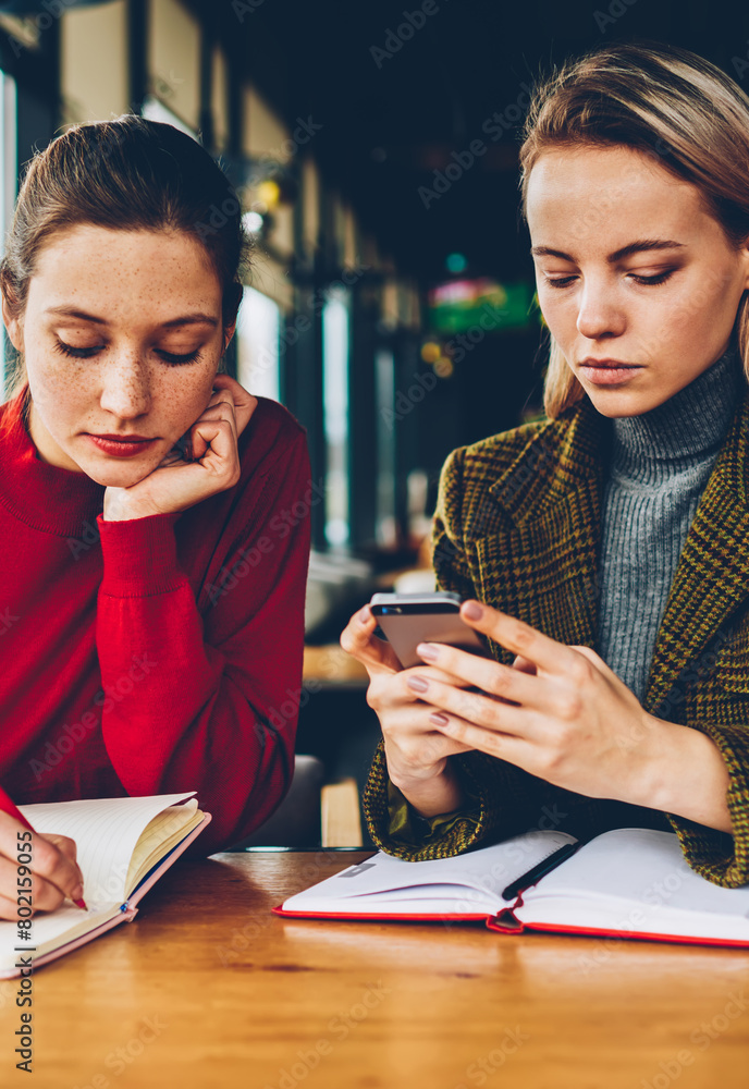 Poster skilled student writing down test in notepad while female tutor reading notification on smartphone d