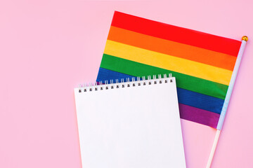 Blank mock up notebook on rainbow LGBTQ flag, pink background. June proud pride month parade, gay...