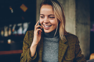 Happy blonde young entrepreneur in elegant jacket calling to best friend and laughing during mobile...