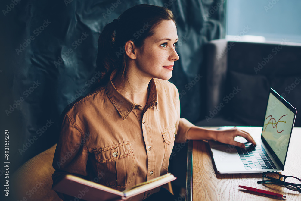 Aufkleber contemplative clever hipster student with studying book in hands sitting at laptop device and workin