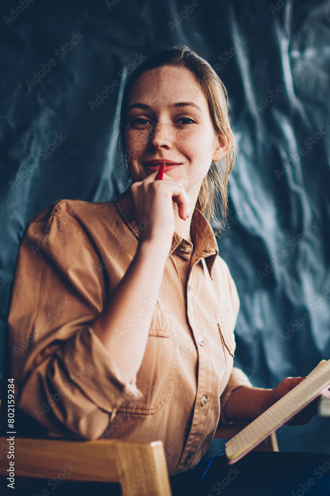 Aufkleber portrait of pretty talented hipster girl with pen in hand looking at camera while sitting with noteb