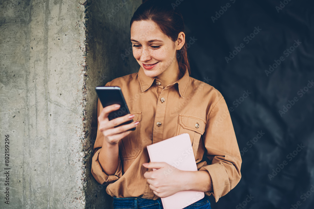 Poster cheerful hipster blogger laughing while updating profile on smartphone device connected to 4g intern