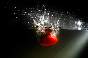 A red bell pepper falls into the water. A splash of water.