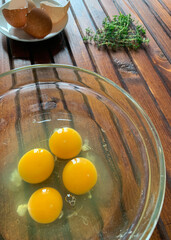 Quattro uova incrinate in una ciotola di vetro isolata su fondo di legno. Cibo salutare. Copia spazio.