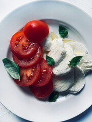 Classica insalata caprese italiana con mozzarella fresca a fette, pomodori, foglie di basilico e olio d'oliva in un piatto bianco. Piatto estivo. Concetto di cibo italiano. Direttamente sopra.