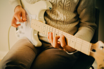 A man wearing a white sweater is playing music on a white electric guitar during a music lesson.