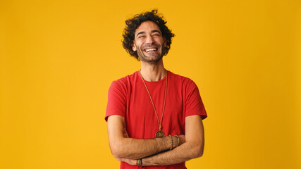 Smiling attractive man with curly hair, dressed in red T-shirt,  crossing his arms and looking at...