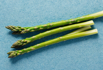 Fresh asparagus tips on a textured sky blue background. AI generated.