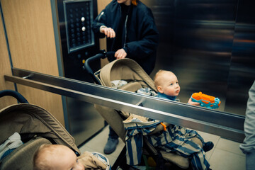 Happy little toddler boy holds toy water gun sitting in a stroller in a elevator