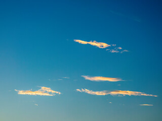 Minimalist cloudscape with slight longitudinal cloudlets drifting in hazy blue sky at sunset in...