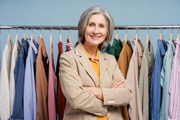 Smiling confident senior woman, stylist, fashion designer standing near clothes rail