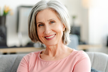 Happy confident senior woman looking at camera sitting on comfortable sofa at home