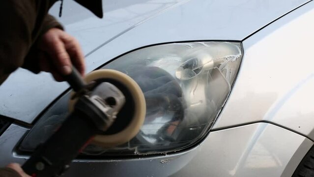 A man polishes a car headlight with a hand grinder.	
