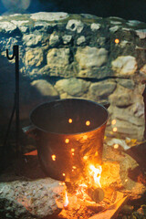 A large, black pot sits atop a crackling fire, the flames swirling and flickering beneath it