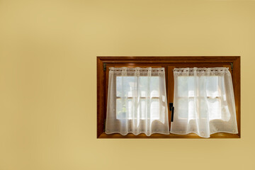 French style wood and glass double sash window with white curtains on a yellow wall