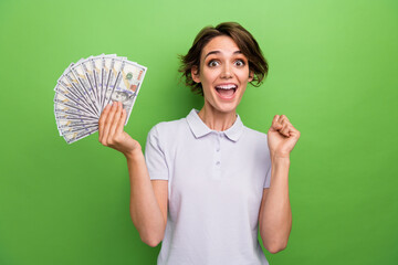 Photo of funky lucky girl dressed grey polo rising fist showing money fan isolated green color...