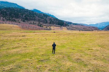 A person stands gracefully in a vast field, surrounded by majestic mountains in the distant...