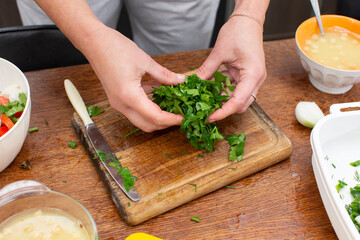 Hands chop parsley on a cutting board. Prepare vegetable salad.