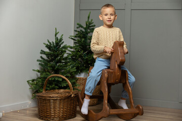 Happy little boy rides on a wooden horse gurney in the Christmas room. - obrazy, fototapety, plakaty