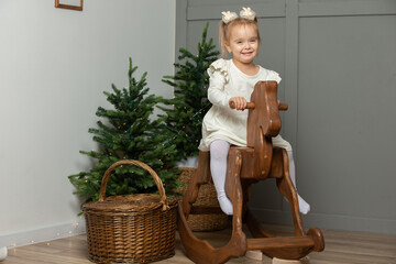 Happy little girl rides on a wooden horse gurney in the Christmas room.