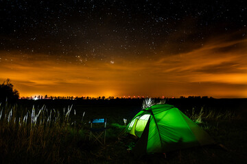 Illuminated tent on a meadow at night. Dark sky with stars and clouds of Sahara dust over Germany....