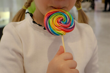 Rainbow-colored colored candy on a stick in the hands of a child, the taste of childhood